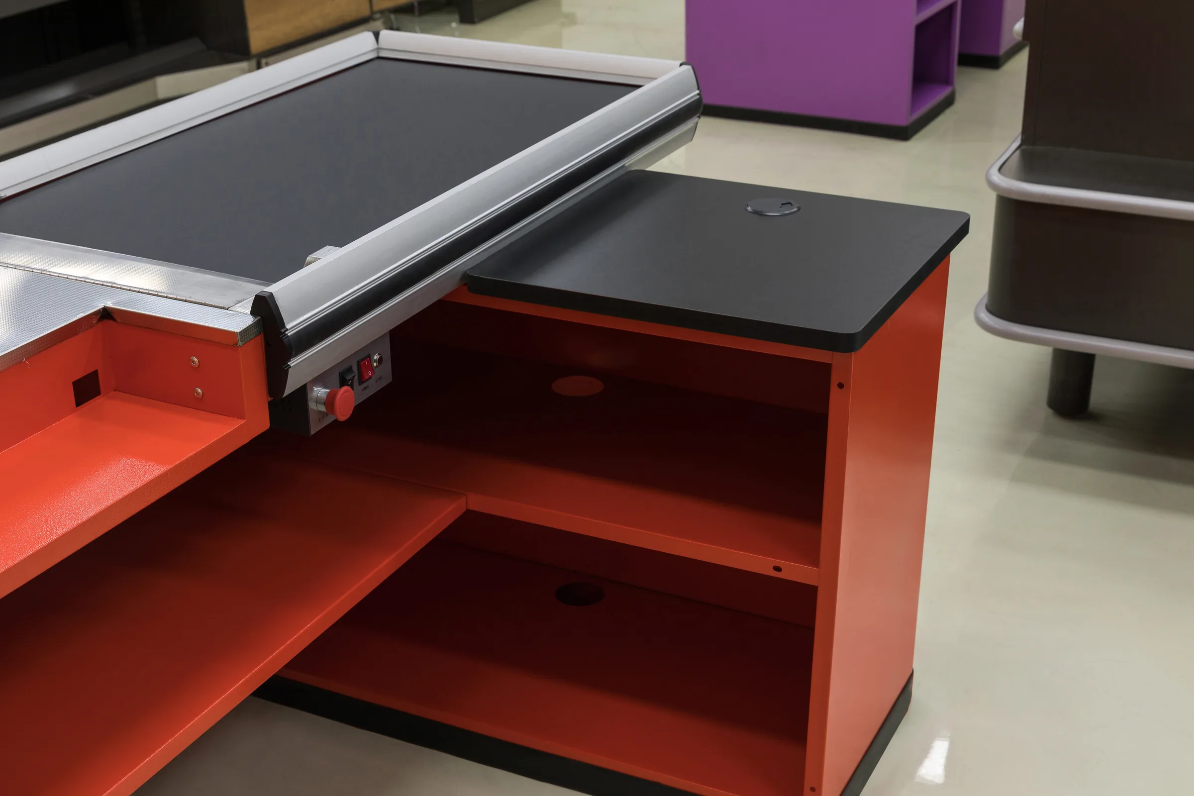 Red Keshun supermarket checkout counter with a conveyor belt and open packing shelf installed on a store floor